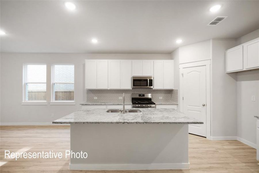 The kitchen features a spacious island with a granite countertop, a stainless steel microwave and oven, and ample cabinetry