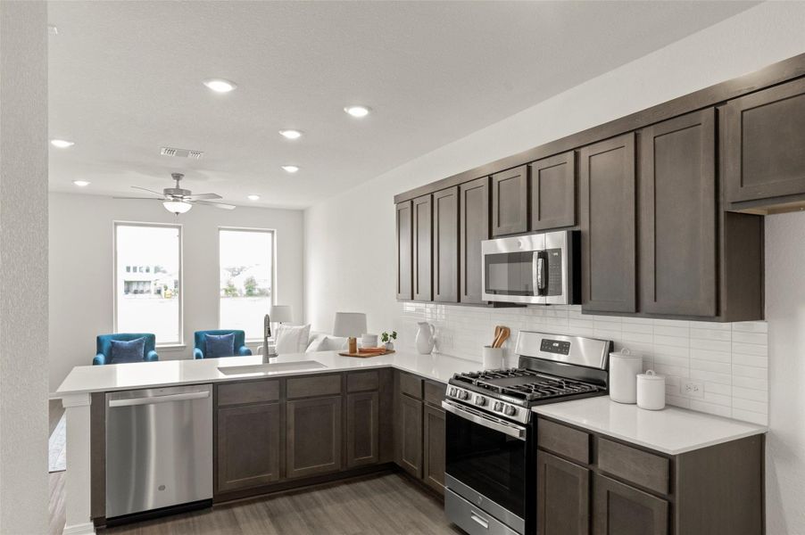 Kitchen featuring stainless steel appliances, a peninsula, light wood-type flooring, light countertops, and backsplash
