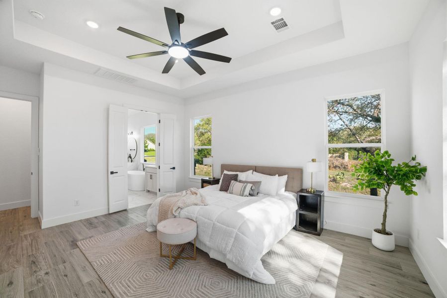 Bedroom with a tray ceiling, light wood-style floors, and recessed lighting Bedroom with a tray ceiling, light wood-style floors, and recessed lighting