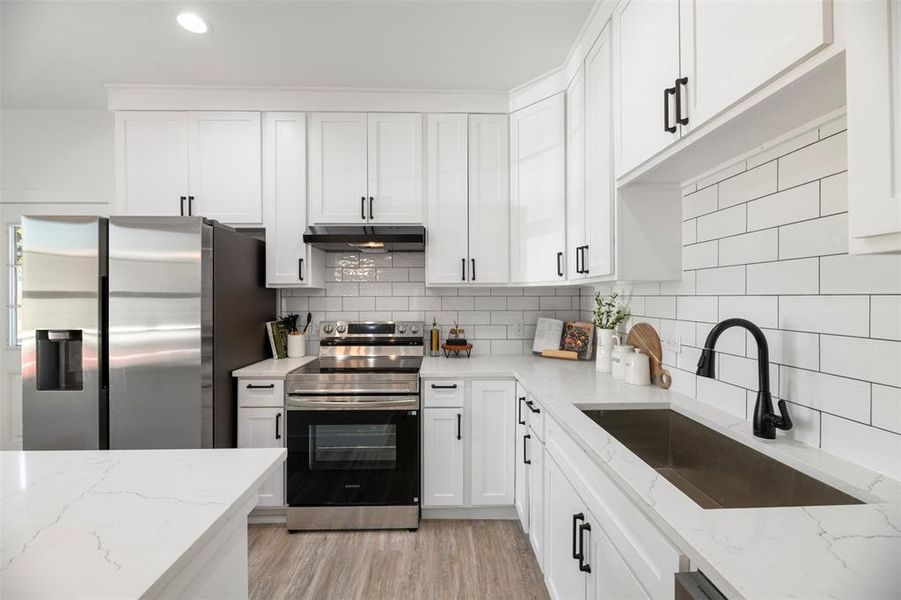 Kitchen with stainless steel appliances, light stone counters, white cabinets, light wood-style floors, and recessed lighting Kitchen with stainless steel appliances, light stone counters, white cabinets, light wood-style floors, and recessed lighting