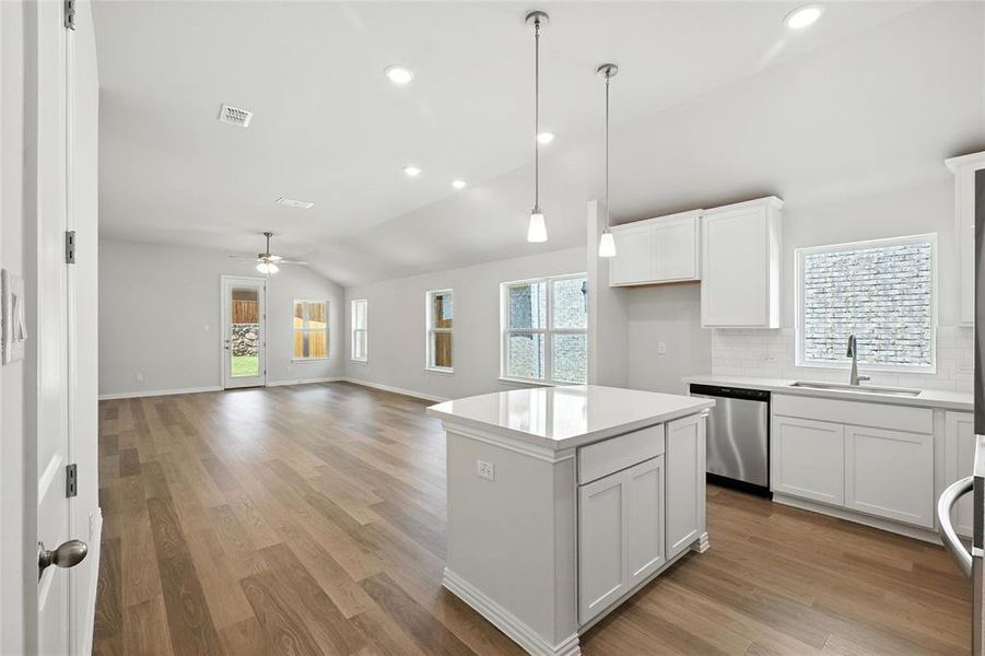 Kitchen featuring light wood-style floors, vaulted ceiling, decorative light fixtures, a center island, and white cabinetry