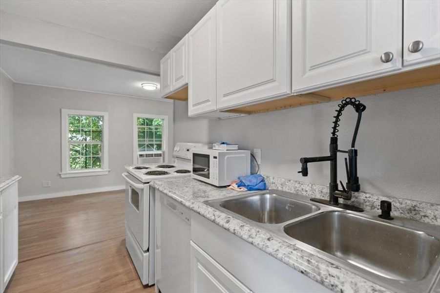 Kitchen featuring light wood-type flooring, white cabinets, light stone countertops, sink, and white appliances Kitchen featuring light wood-type flooring, white cabinets, light stone countertops, sink, and white appliances