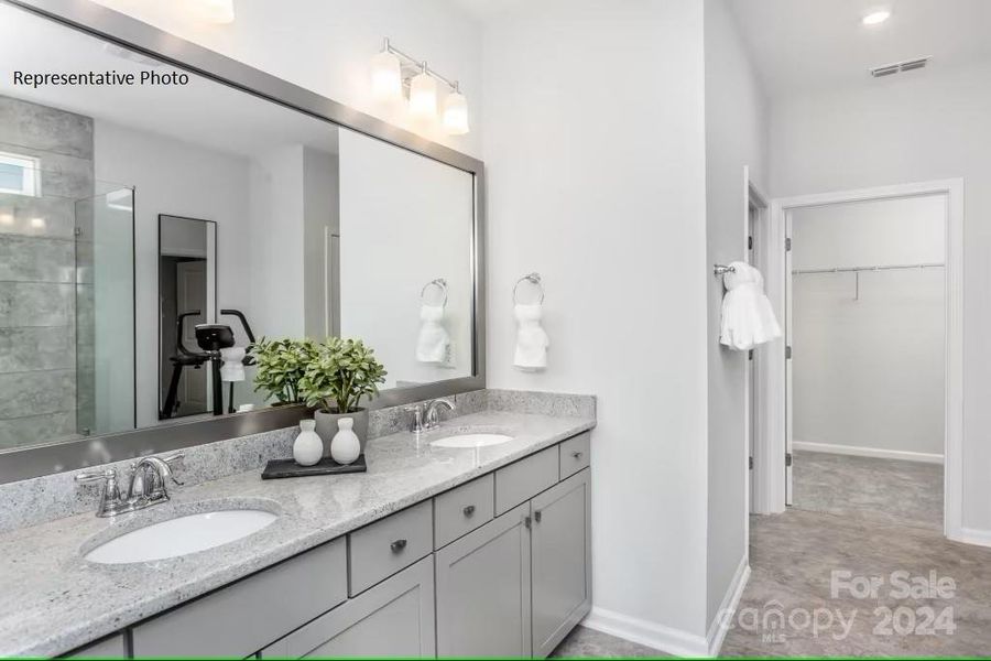 First-floor owner's bathroom features dual sinks and an oversized, zero-entry shower, adjoining a walk-in closet