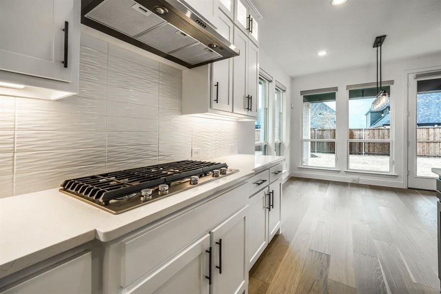 Kitchen with decorative backsplash, light countertops, exhaust hood, and stainless steel gas cooktop