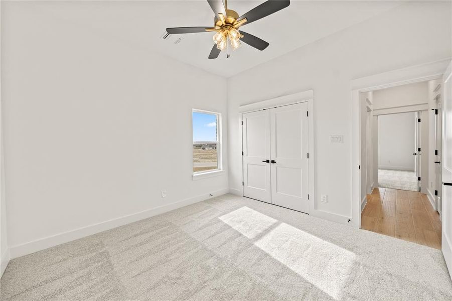 Neutral-toned carpeting in a room featuring a window with an outdoor landscape, a ceiling fan with integrated lighting, and white double closet doors with black hardware