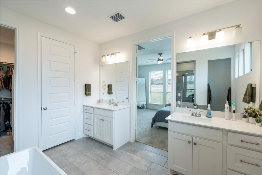 Bathroom with ensuite bath, two vanities, a freestanding tub, ceiling fan, and light colored carpet
