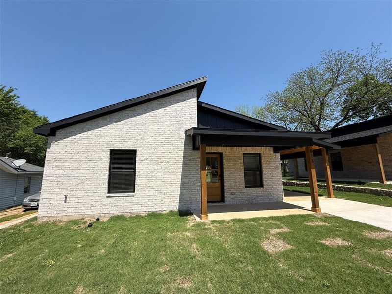 View of front of home with a front yard, brick siding, a patio area, and board and batten siding View of front of home with a front yard, brick siding, a patio area, and board and batten siding