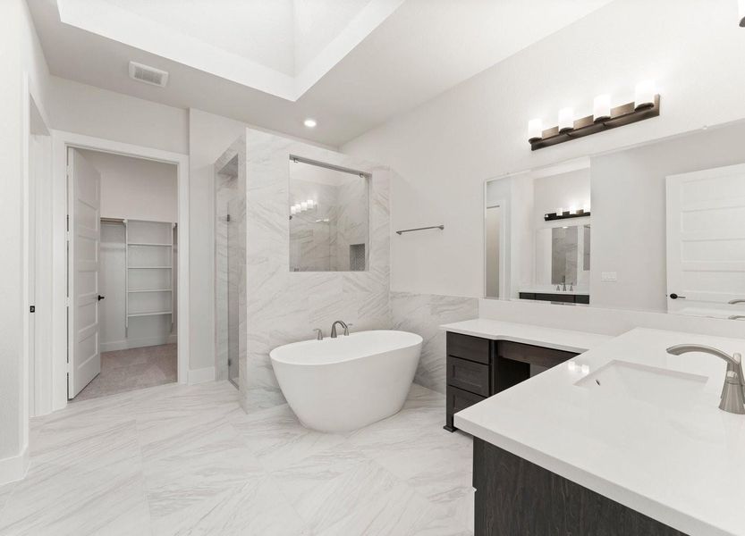 This bathroom features a sleek, modern design with a freestanding bathtub, spacious walk-in shower, double vanity, and stylish lighting. The neutral tones create a calming atmosphere, and there's a walk-in closet accessible from the bathroom.