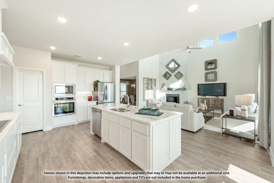 Open-concept kitchen with white cabinets, center island, and stainless appliances flowing into a living room with fireplace.