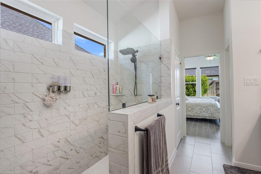 Luxurious bathroom featuring a sleek walk-in shower with elegant tiles and modern fixtures, seamlessly connecting to a bright bedroom with garden views.