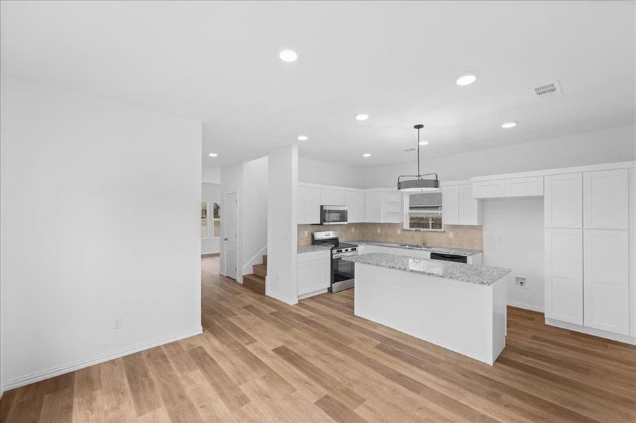 Spacious kitchen and dining area featuring granite countertops, white cabinetry, stainless steel appliances, and recessed lighting. Island offers additional prep space and seating.