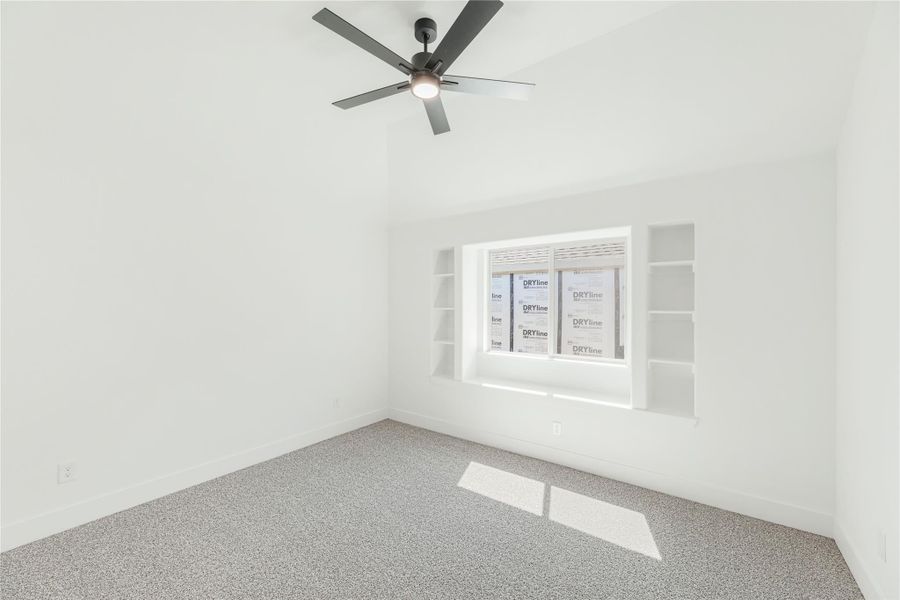 Empty bedroom with gray carpet, ceiling fan, vaulted ceiling, and built-in shelves flanking a window Empty bedroom with gray carpet, ceiling fan, vaulted ceiling, and built-in shelves flanking a window