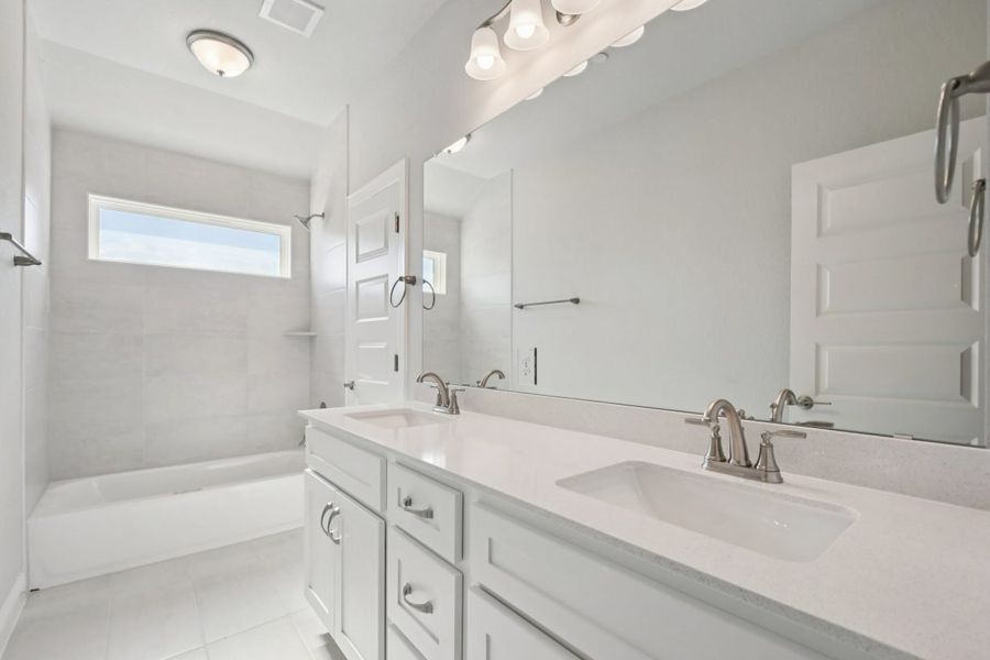 Image of a bathroom with a white jack and jill vanity, white cabinets, a large mirror, a shower with a white tub and a window above
