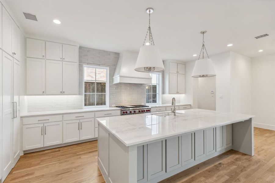 Kitchen with light hardwood flooring, white cabinets, and an island with sink