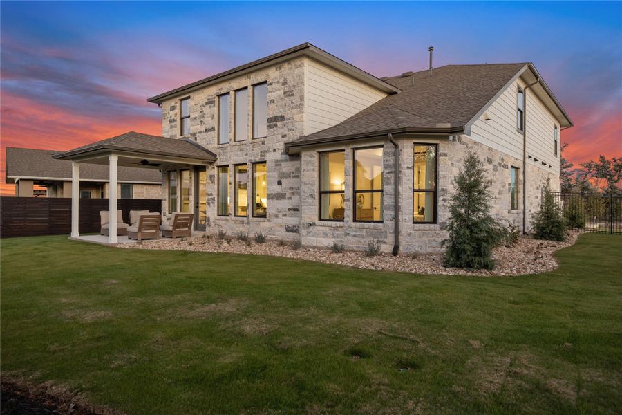 Back of property at dusk with a patio, outdoor lounge area, a shingled roof, and stone siding
