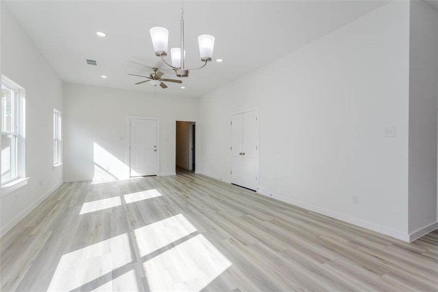 Empty room featuring light wood-type flooring and ceiling fan with notable chandelier