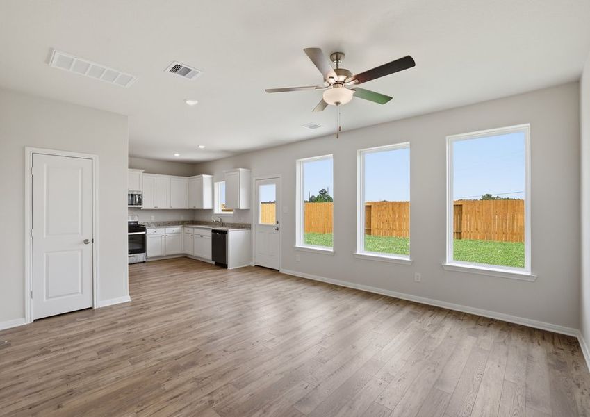 Family room looking toward the kitchen, featuring wood-look vinyl flooring and large backyard-facing windows.