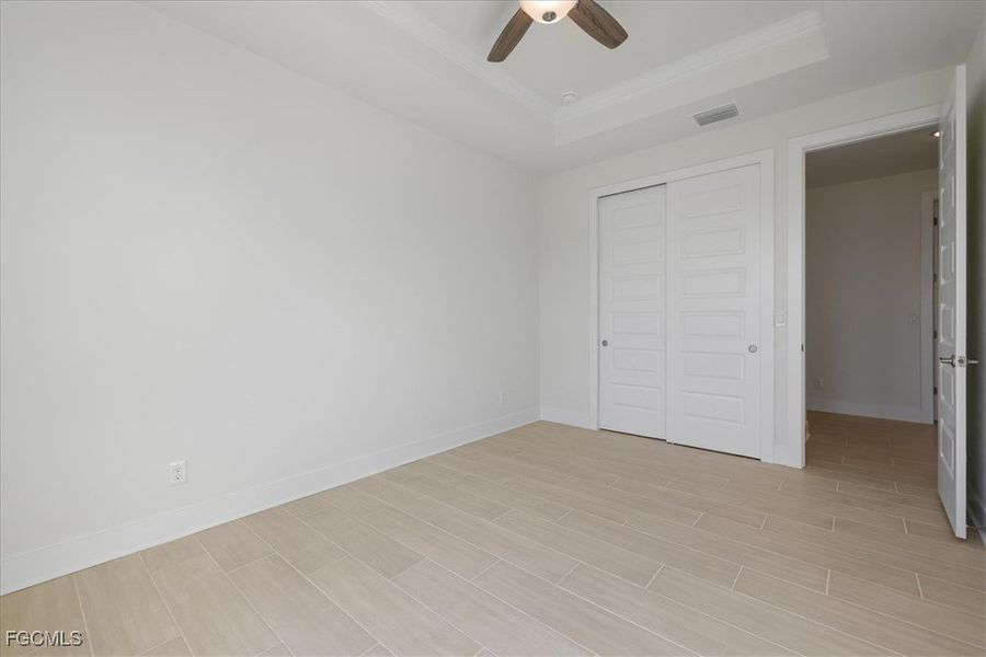 Unfurnished bedroom featuring a closet, a ceiling fan, a tray ceiling, and wood finish floors
