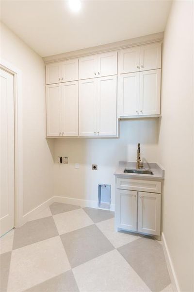 Utility room featuring extensive white cabinetry with crown molding, a built-in sink with a brushed nickel faucet, a light-toned countertop, and a checkered floor pattern