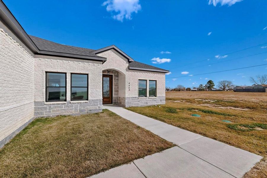 Property entrance featuring brick siding, a lawn, and a shingled roof