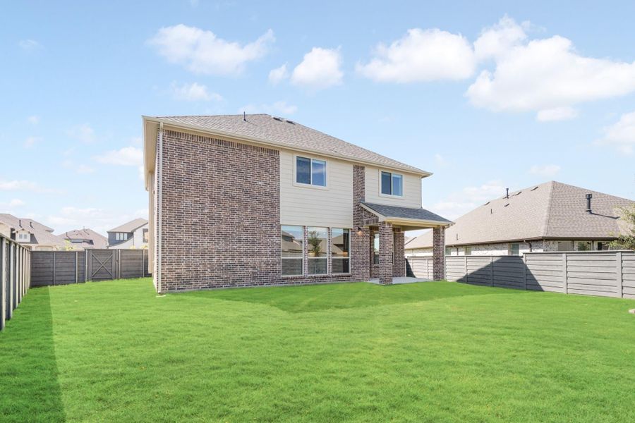 Two-story brick home with covered patio, large fenced backyard, and green lawn viewed from rear