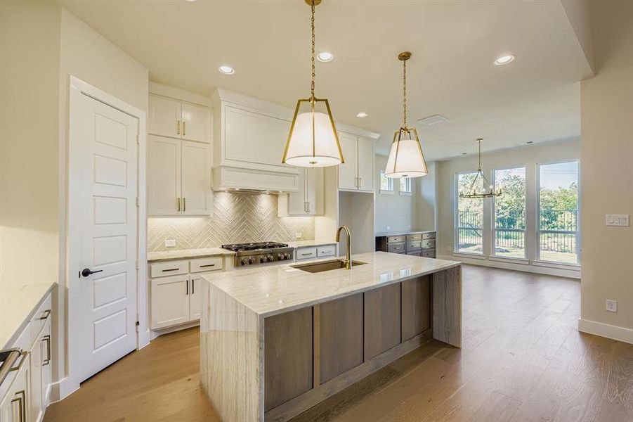 Kitchen featuring light stone counters, decorative backsplash, a kitchen island with sink, recessed lighting, and decorative light fixtures