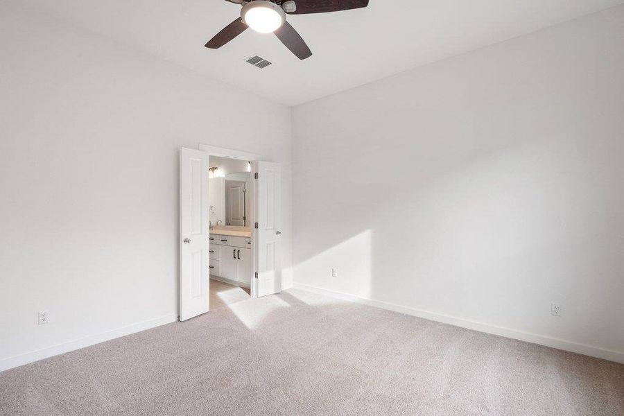Unfurnished bedroom featuring light colored carpet, ensuite bathroom, and a ceiling fan
