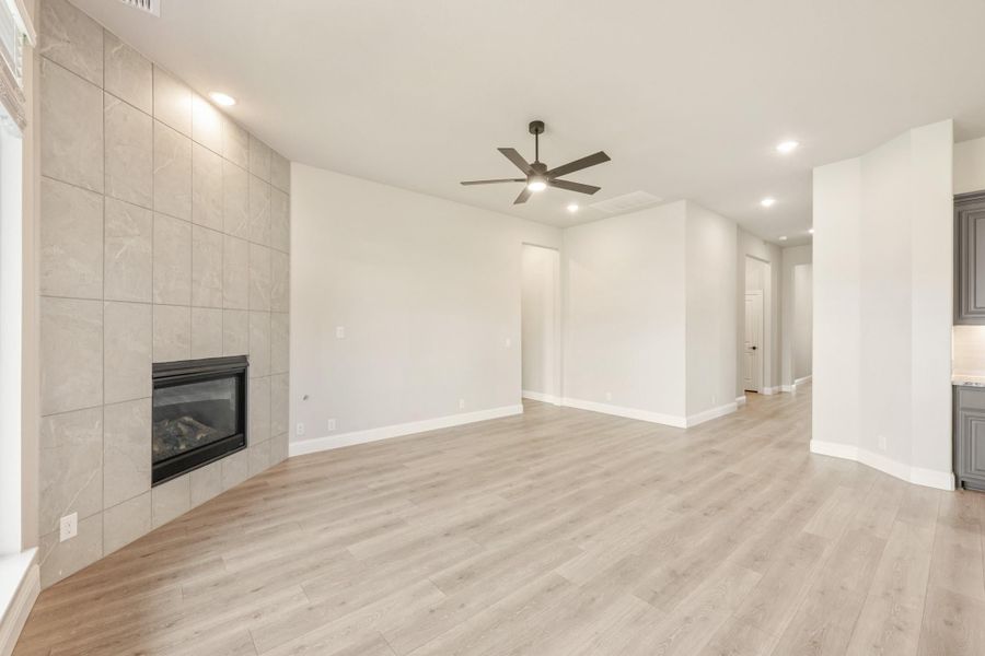 Open living room with tile-surround fireplace, light wood floors, and ceiling fan Open living room with tile-surround fireplace, light wood floors, and ceiling fan