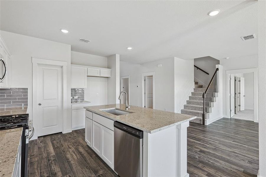 Kitchen with decorative backsplash, dishwasher, gas stove, sink, and a center island with sink