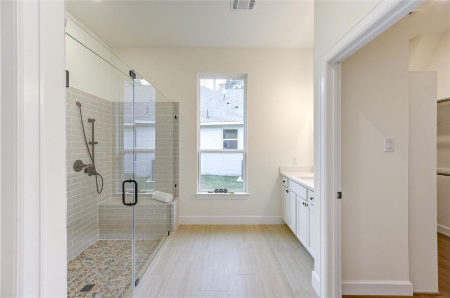 This bathroom features a spacious walk-in shower with a glass door and stone floor, a large window providing natural light, and a sleek vanity with ample storage. This bathroom features a spacious walk-in shower with a glass door and stone floor, a large window providing natural light, and a sleek vanity with ample storage.