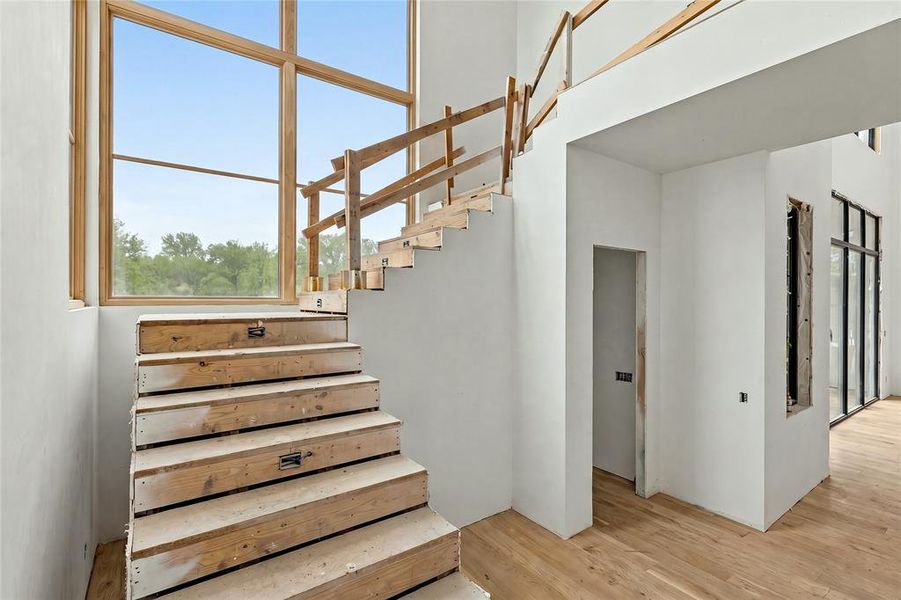 Two-story interior featuring a spacious open concept, large wood-frame windows, light wood-finish flooring, and a multi-level staircase