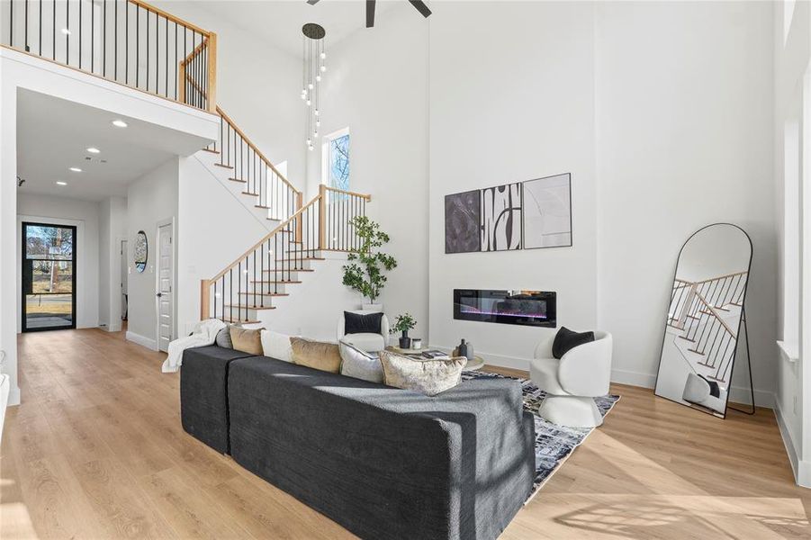 Living area featuring a glass covered fireplace, light wood-type flooring, a high ceiling, and a ceiling fan