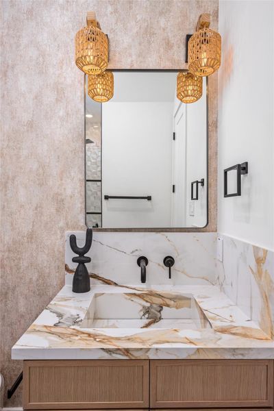 The guest bath features an onsite-crafted porcelain sink, accent mirror, luxe vanity lighting, and designer fixtures throughout