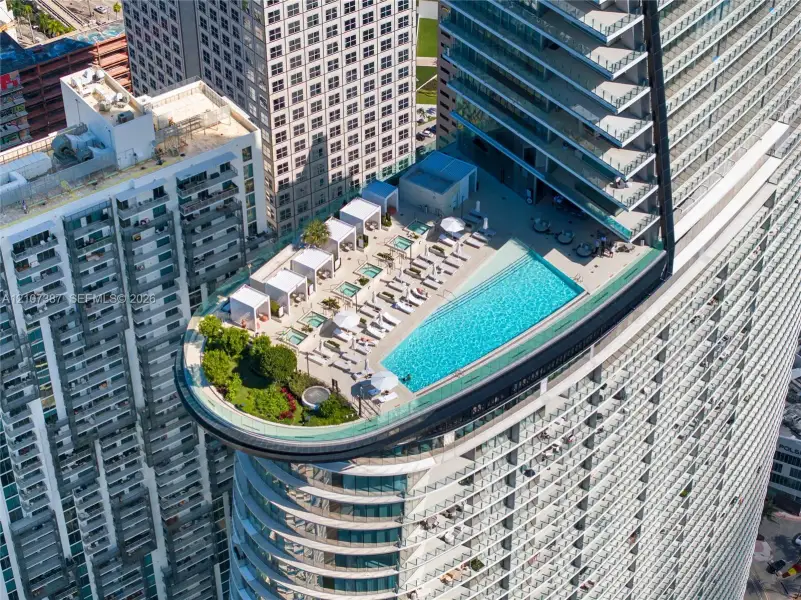 Rooftop terrace featuring an infinity-edge pool, integrated hot tubs, structured cabanas, glass railings, and landscaped green space