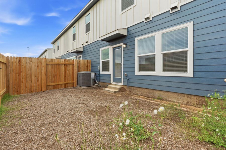 Private outdoor space featuring a wood fence, a rear entry door, and two large windows Private outdoor space featuring a wood fence, a rear entry door, and two large windows