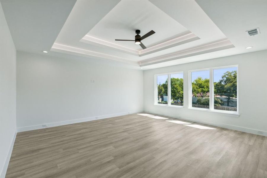 Living room flex space with ceiling fan, a raised ceiling, and light hardwood / wood-style floors