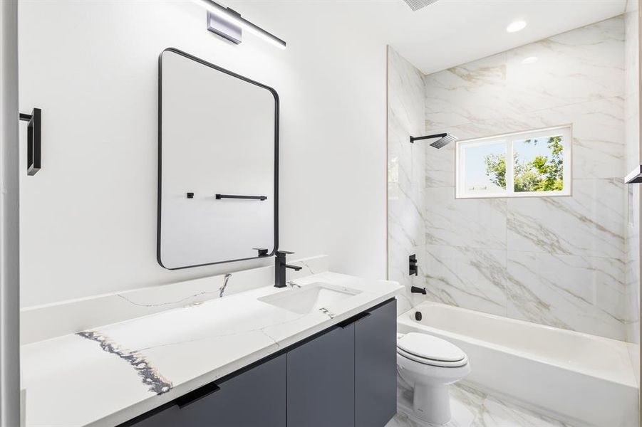 Bathroom featuring a modern vanity with dark cabinetry, integrated sink, and a stone-finish countertop Bathroom featuring a modern vanity with dark cabinetry, integrated sink, and a stone-finish countertop