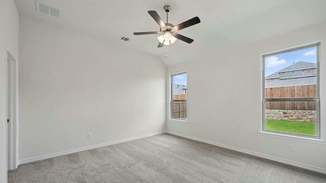 Carpeted interior room featuring two windows with outdoor scenery, vaulted ceilings, and a ceiling fan with integrated lighting