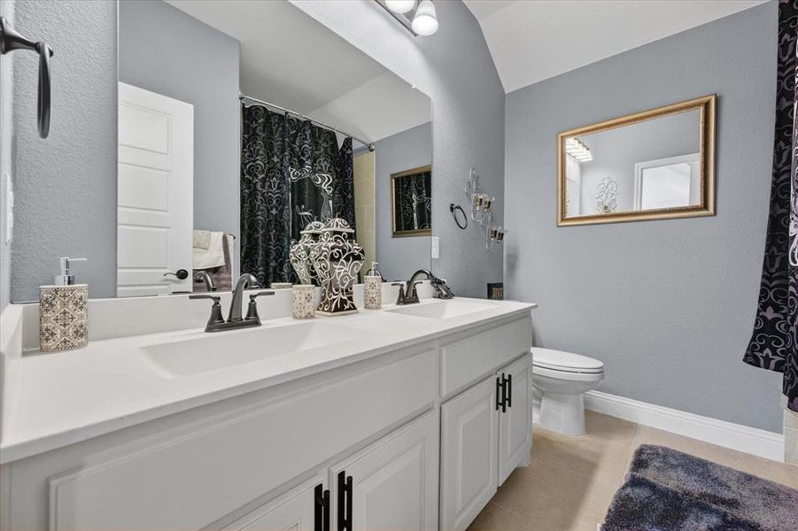 Full bathroom with double vanity, light tile patterned flooring, a shower with curtain, and a textured wall Full bathroom with double vanity, light tile patterned flooring, a shower with curtain, and a textured wall