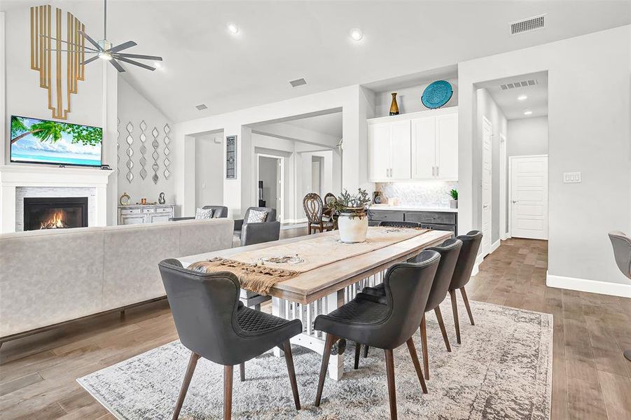 Dining area with light wood-style floors, a glass covered fireplace, a ceiling fan, recessed lighting, and lofted ceiling