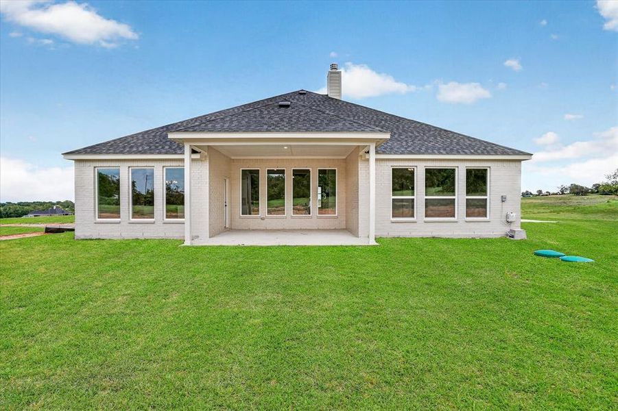 Expansive rear facade featuring a covered patio, multiple large windows, and a shingle roof