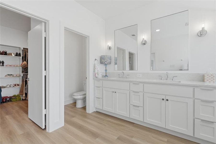 Bathroom featuring a dual vanity with white shaker-style cabinetry, a light-toned countertop, and individual mirrors with sconce lighting