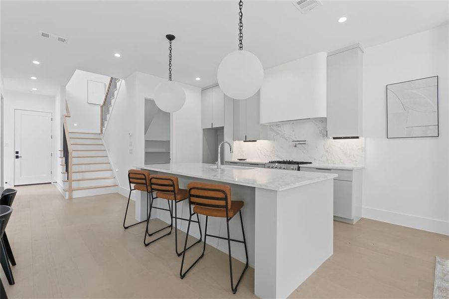 Modern kitchen featuring a waterfall island with a stainless steel sink, a gas range with a pot filler, marble-look slab backsplash, recessed lighting, and wood-finish flooring