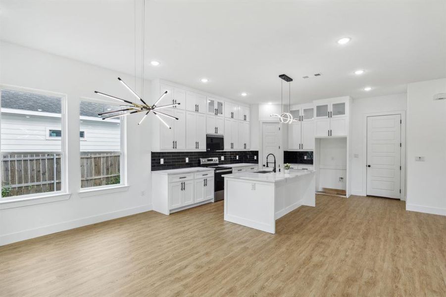 Kitchen featuring decorative backsplash, light wood-type flooring, an island with sink, and stainless steel electric stove