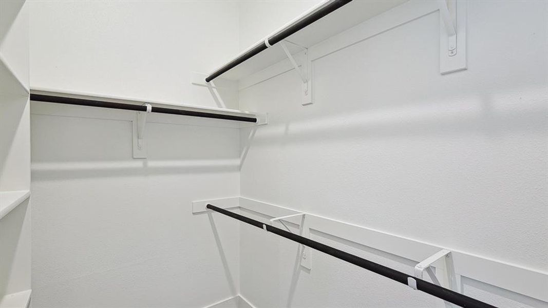 Walk-in closet featuring white walls, integrated shelving, and multiple hanging rods