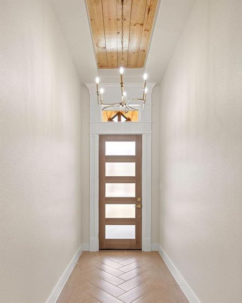 Doorway with wooden ceiling, baseboards, and a chandelier