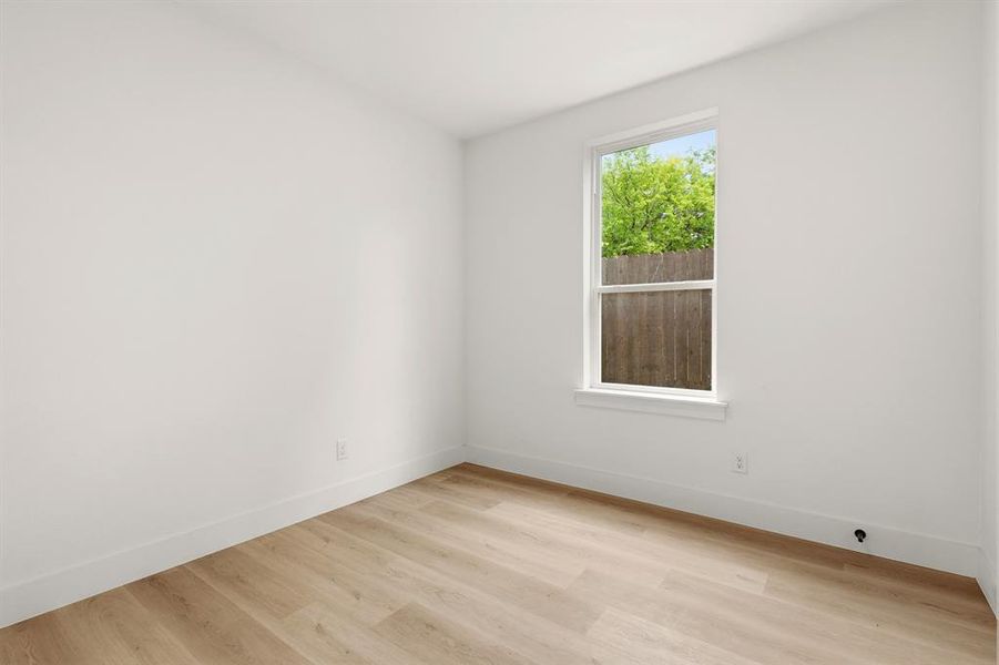 This room features light-toned wood flooring, clean white walls, and a window providing natural light and a view of exterior trees and a wooden fence