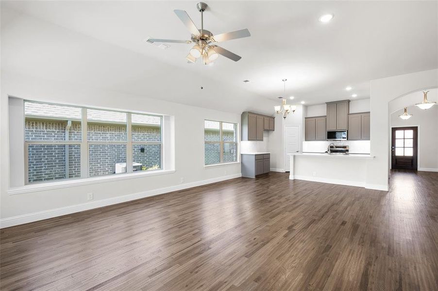 Unfurnished living room with dark wood-type flooring, healthy amount of natural light, recessed lighting, a chandelier, and a ceiling fan