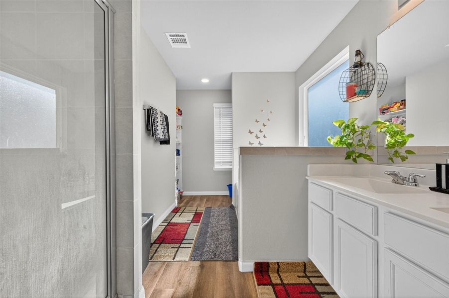This bathroom features a modern design with a glass-enclosed shower, dual sinks with white cabinetry, and ample natural light. The space is accented with plants and decorative touches, creating a welcoming and functional environment.
