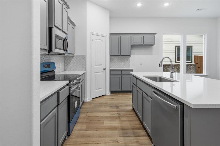 Kitchen with gray cabinetry, stainless steel appliances, light wood-style floors, light stone counters, and recessed lighting
